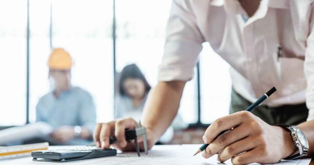 A close-up of an engineer or consultant working on a technical blueprint with a pencil and calculator, symbolizing the detailed technical design and implementation phase of AI Consulting Services.